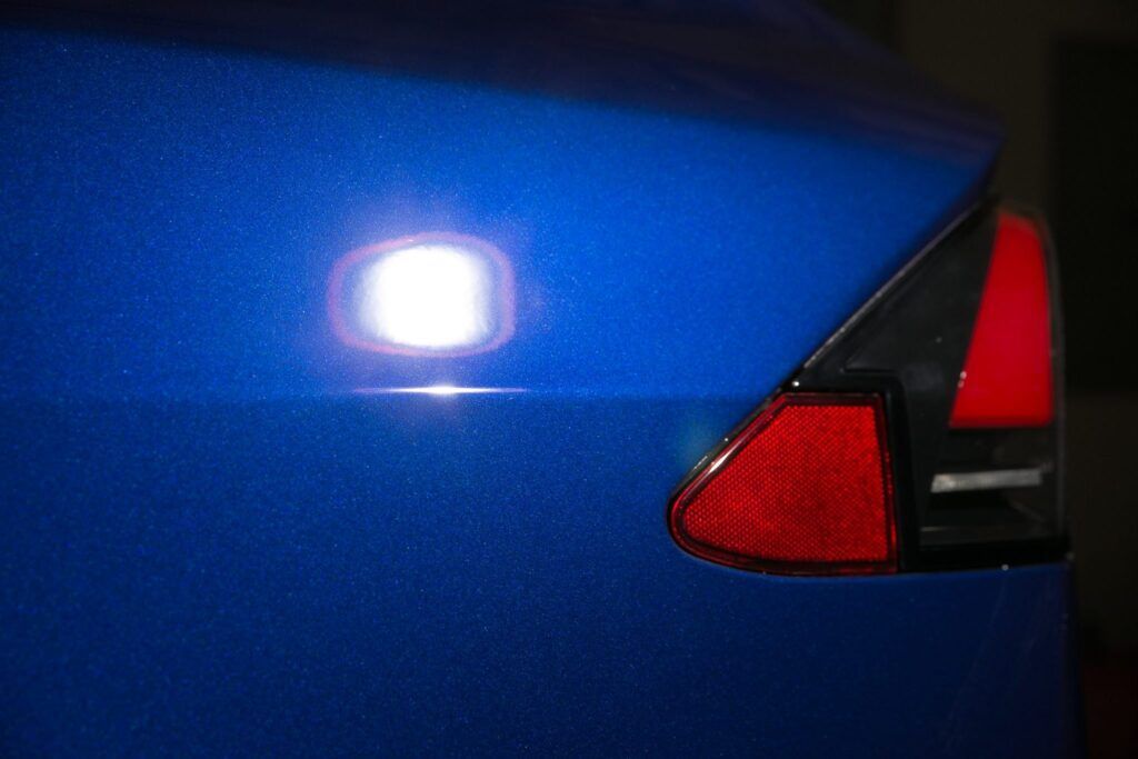 Blue car rear with a taillight, reflecting a bright light.