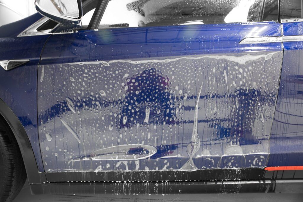 Blue car door with protective film being applied, wet with soapy water.