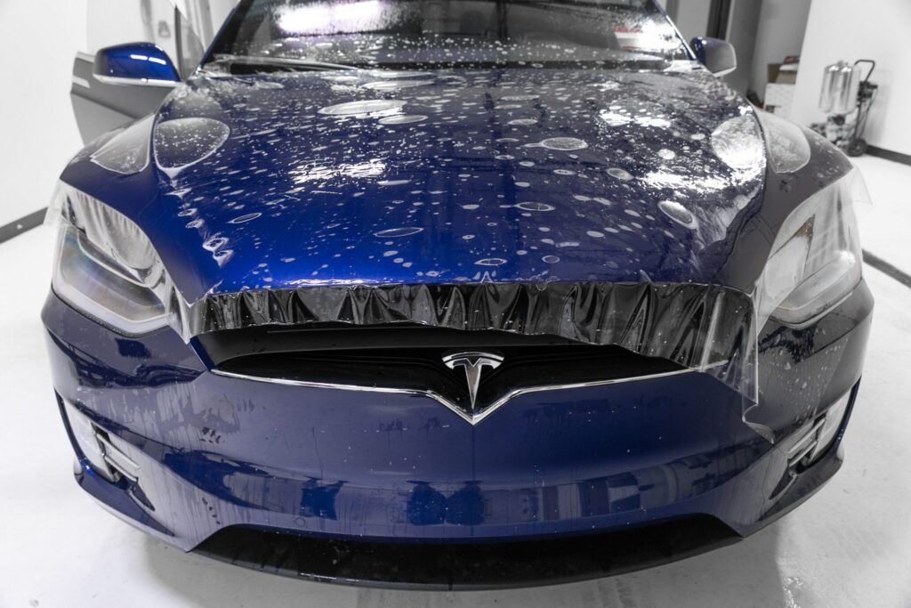 Blue Tesla car front with water droplets.