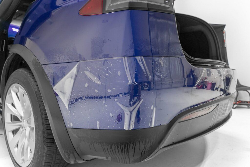 Blue Tesla car with clear protective film applied to rear bumper.