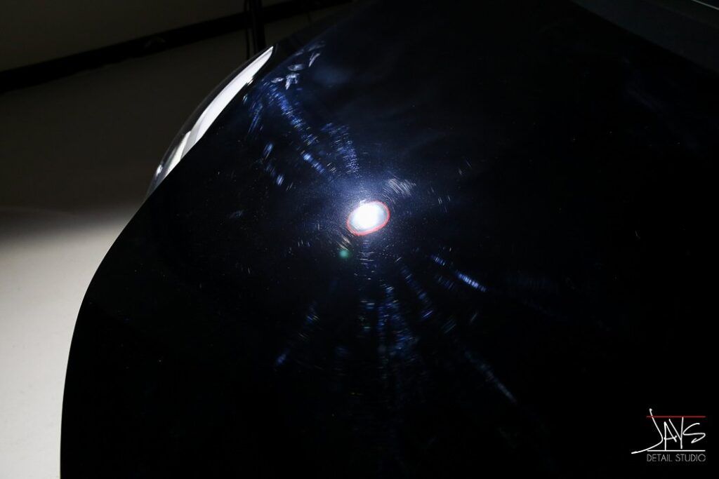 Black car hood with scratches reflecting light.