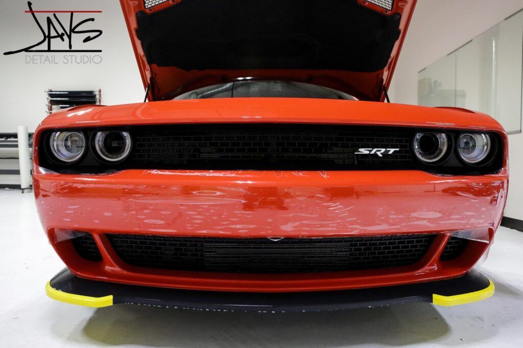 Red Dodge Challenger with hood open, displaying black grille and yellow-trimmed splitter.