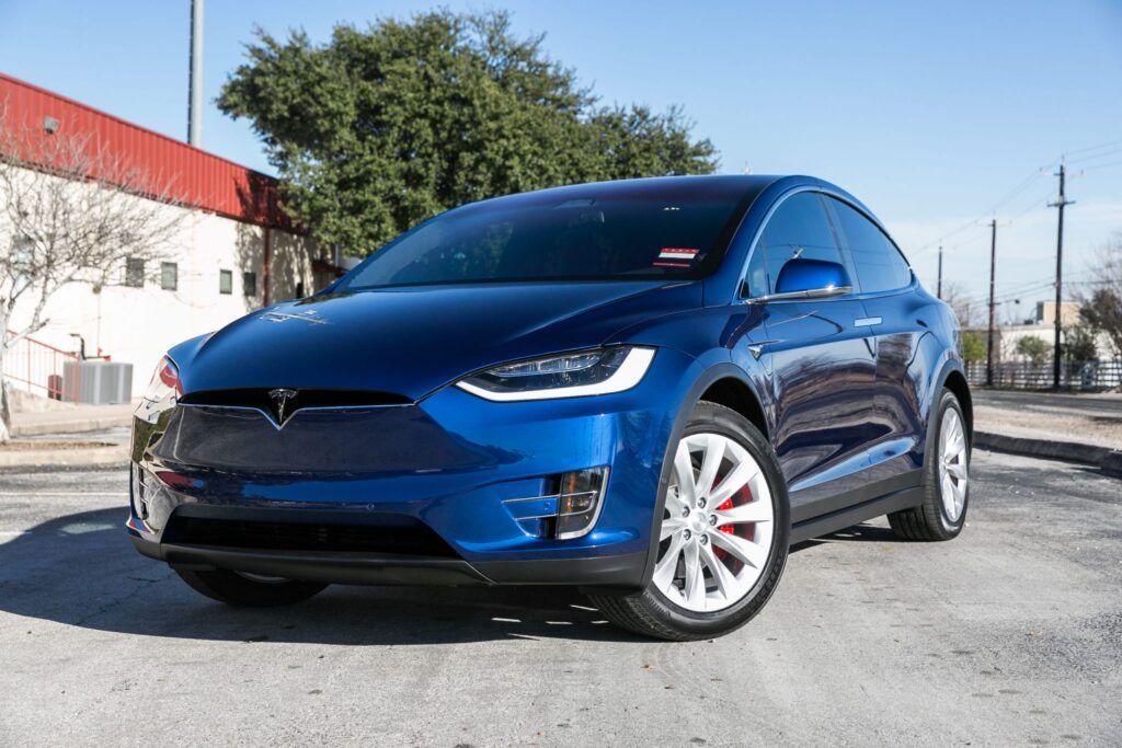 Blue Tesla Model X SUV parked on a sunny street.
