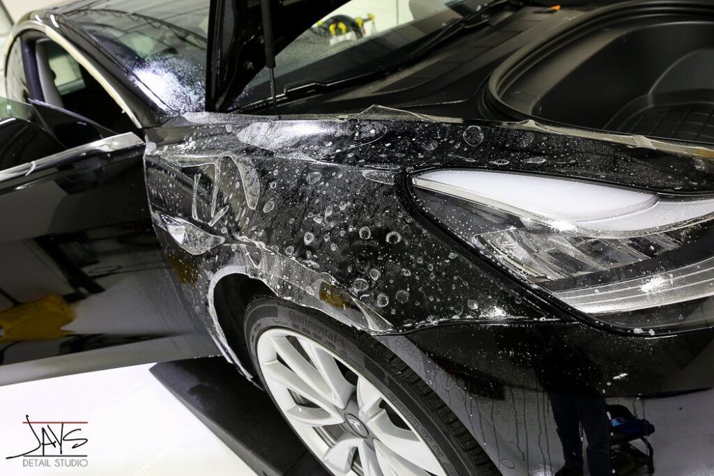 Black car being coated with bubbles, likely for paint protection film application.