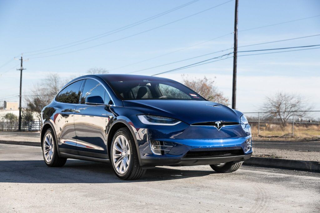 Blue Tesla Model X SUV parked on a paved road under a clear sky.