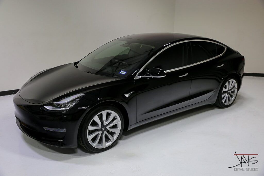 Black Tesla Model 3 sedan, on display in a showroom, silver wheels, tinted windows.