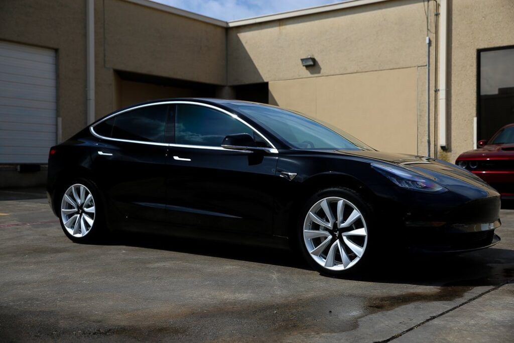 Black Tesla Model 3 parked outside a building on a sunny day.