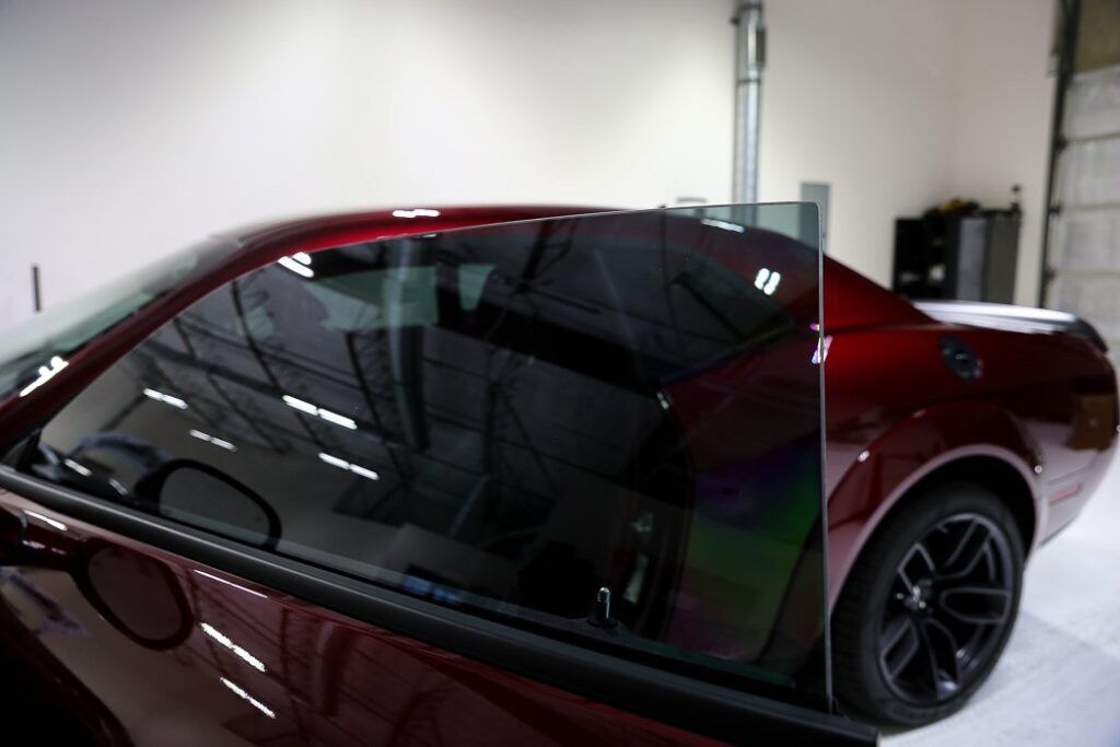 Red car with tinted windows, partially obscured by a glass sheet, in a garage.