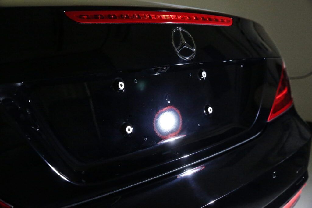 Black Mercedes-Benz car rear with bright license plate light, red brake light.
