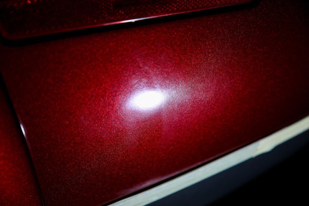 Close-up of a shiny, dark red car surface reflecting light, with white trim visible at the bottom.