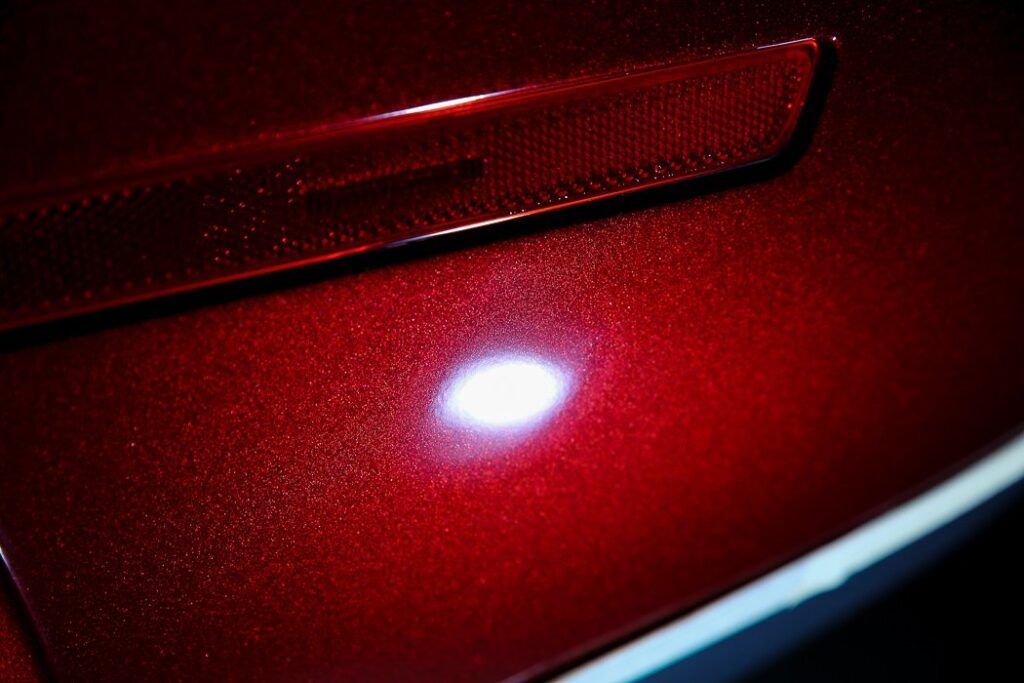 Red car paint with visible scratches reflecting light.