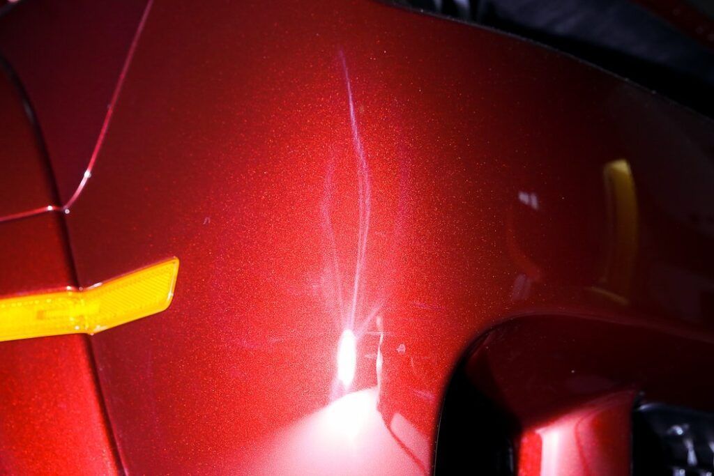 Red car panel with scratches and a yellow light.