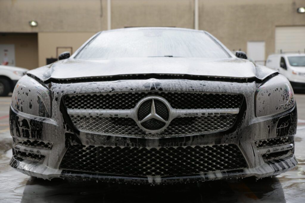 Mercedes-Benz car covered in foamy soap suds at a car wash.