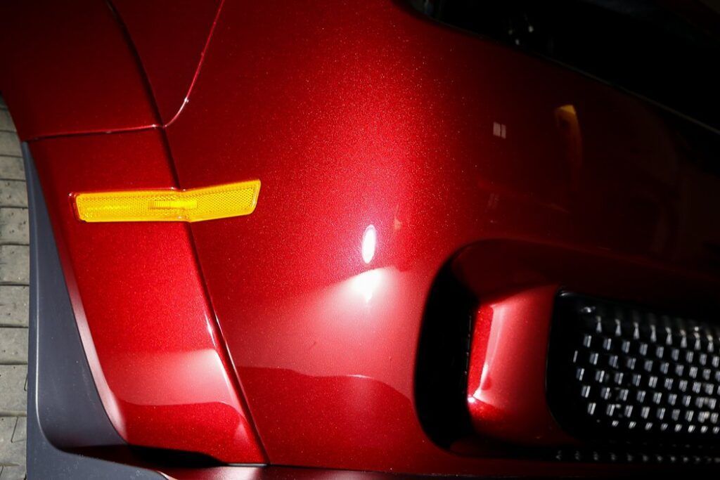 Red car's front bumper with a side marker light and black grill.