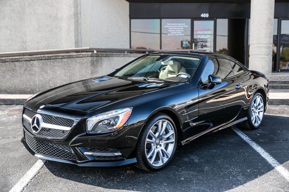 Black Mercedes-Benz SL convertible parked in front of a building with bright wheels.