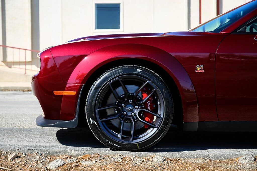 Red Dodge Challenger car front wheel, black rim, red brake caliper, on street.