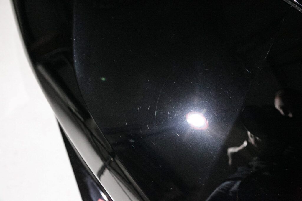 Black car paint with visible scratches reflecting a bright light.