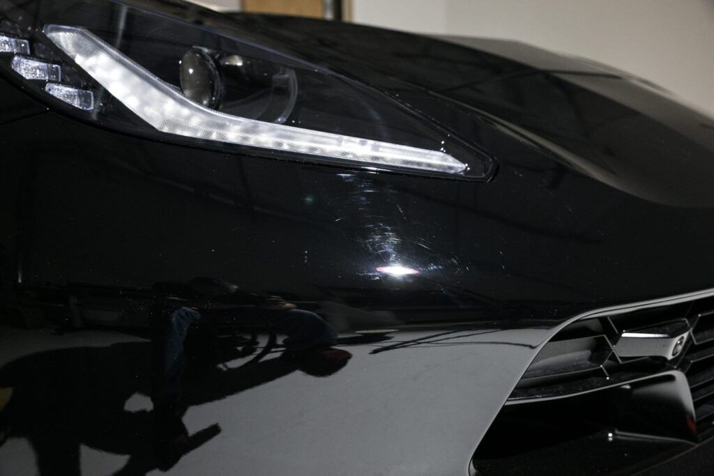 Black car's front with headlight lit. Small paint imperfections are visible.