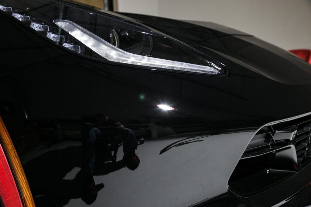 Black sports car's front with bright headlight and reflection of person.