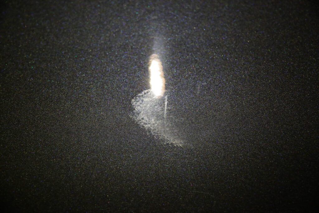 A vertical white streak with a fuzzy base on a dark textured surface.