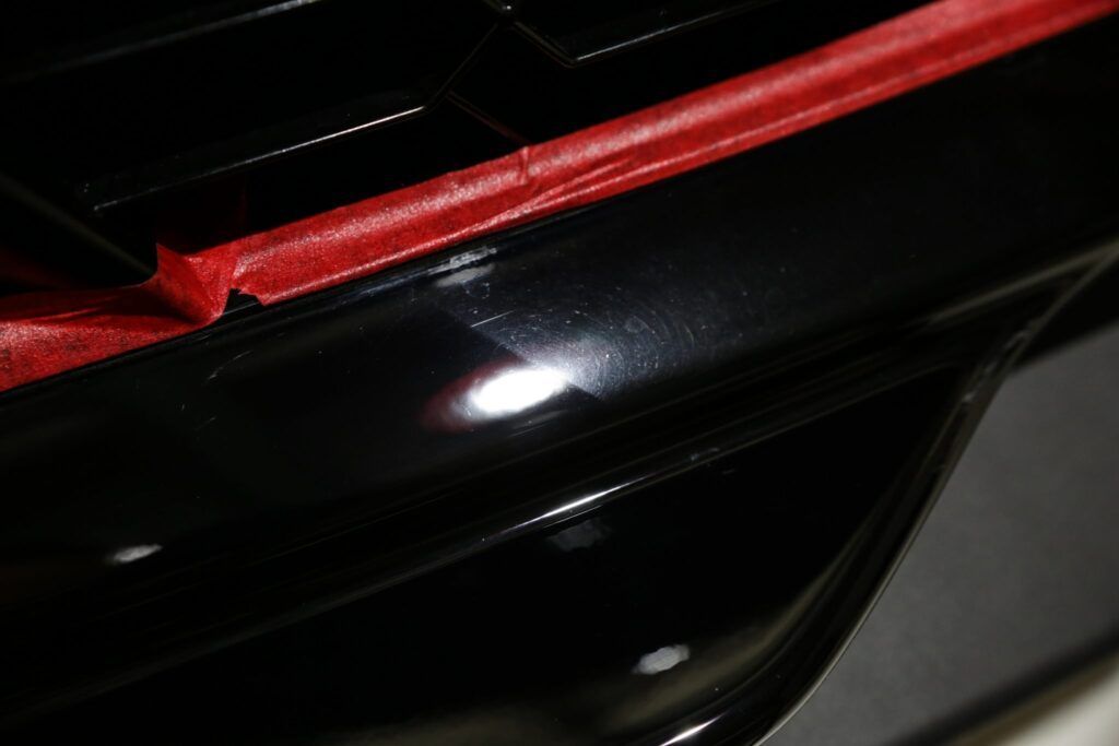 Black car paint with red tape, showing swirl marks before polishing.