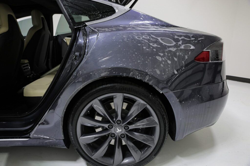 Gray Tesla car with open door; wet film on the body.