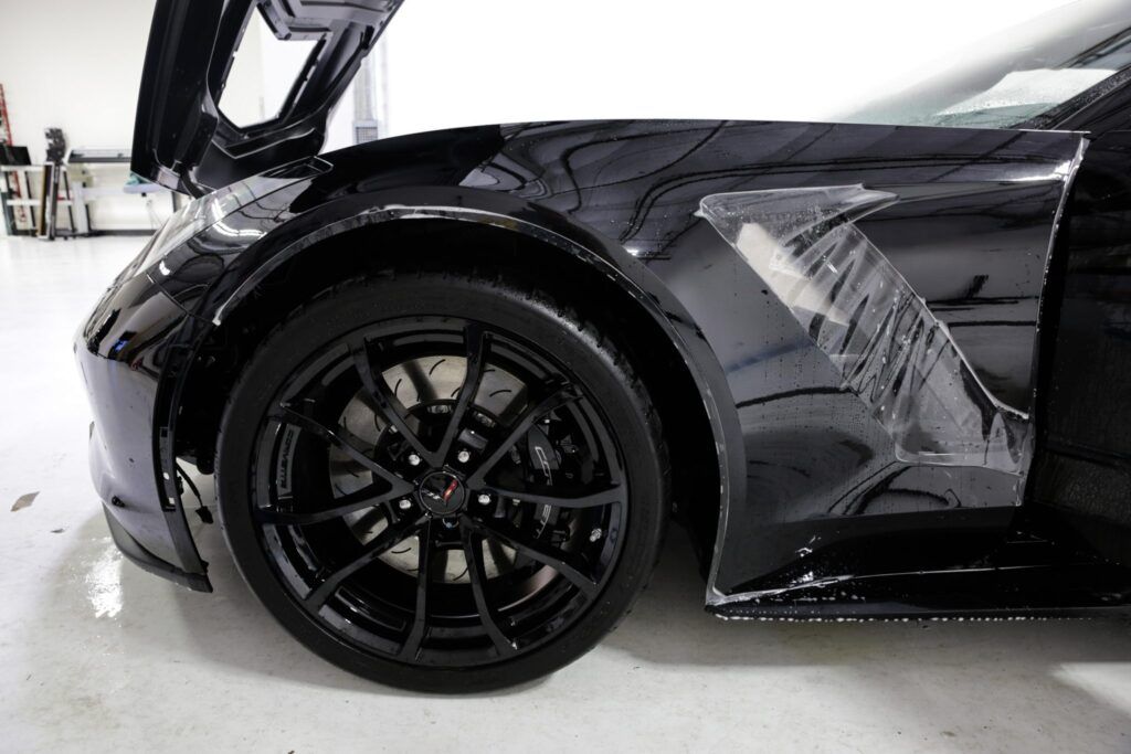 Black sports car with wheel, front fender, and open door. Clear protective film applied.