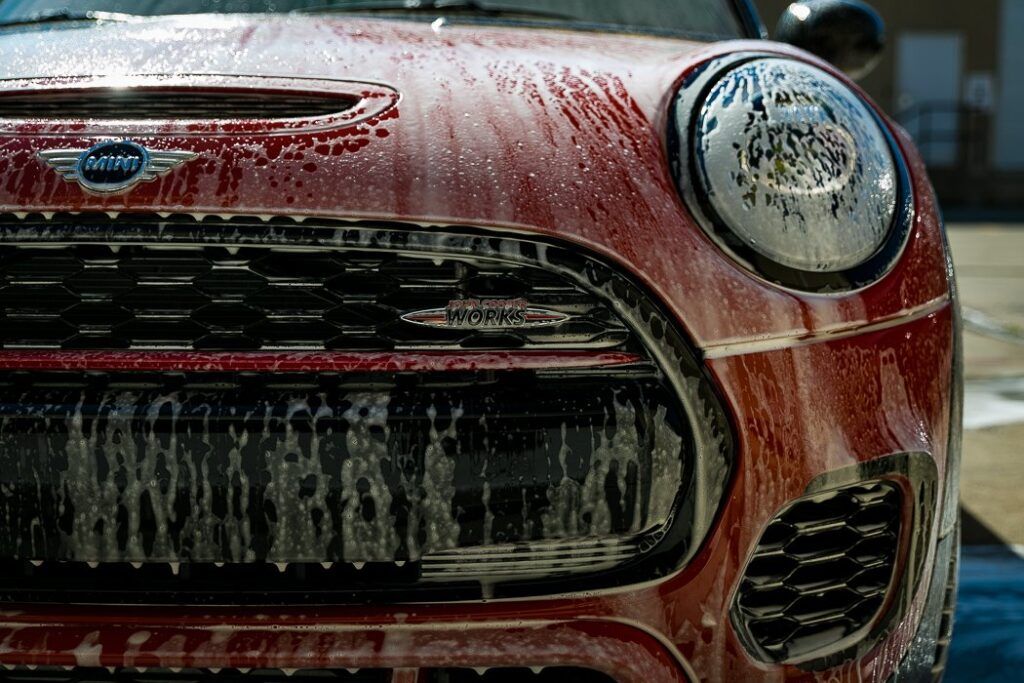 Red Mini Cooper being washed, covered in foamy soap.