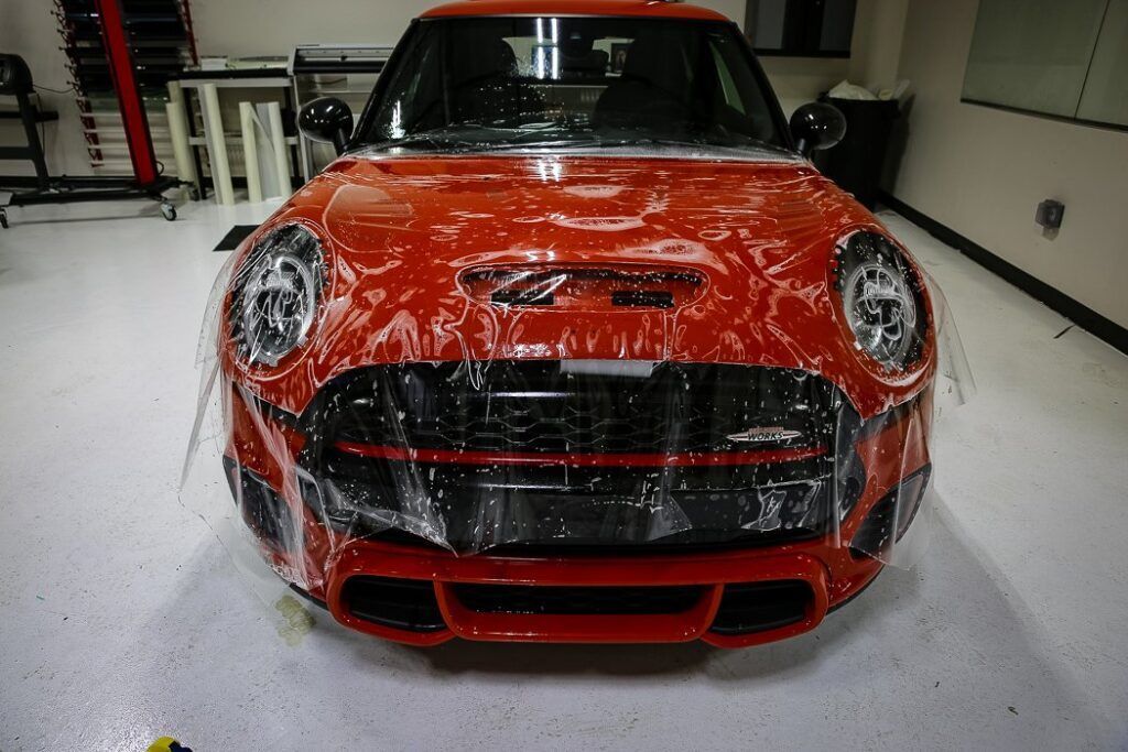 Red Mini Cooper with protective film applied to its front, indoors.
