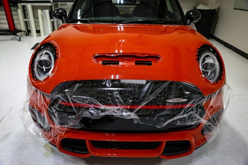 Orange Mini Cooper with protective film on the front, indoors.