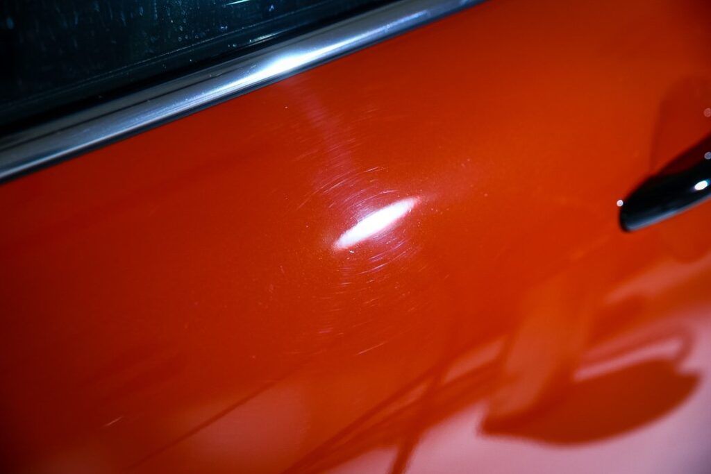 Orange car door with minor scratches reflecting light.