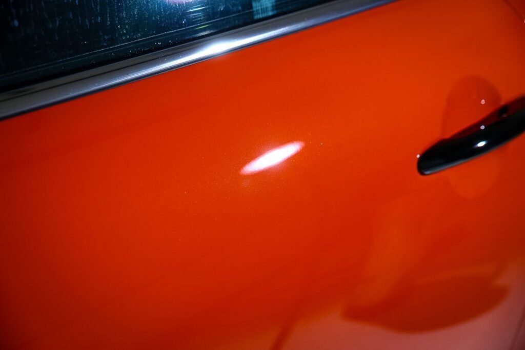 Orange car door with a white scratch, black handle, and a window frame.