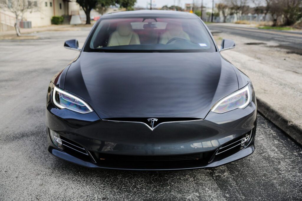 Dark gray Tesla car parked on asphalt, with white interior visible.