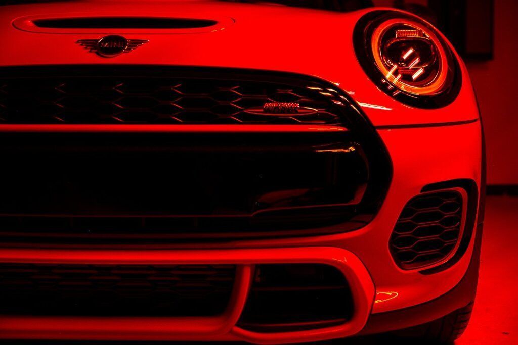 Close-up of a red MINI Cooper front end, highlighting the grill, headlights, and logo.