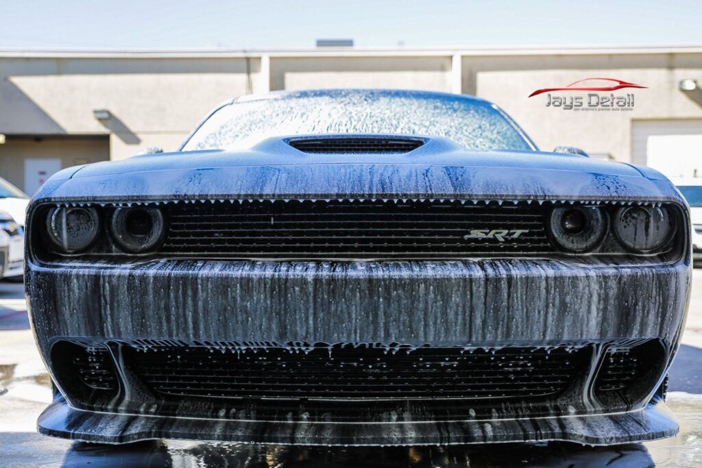 Black Dodge Challenger covered in soapy foam at a car wash.