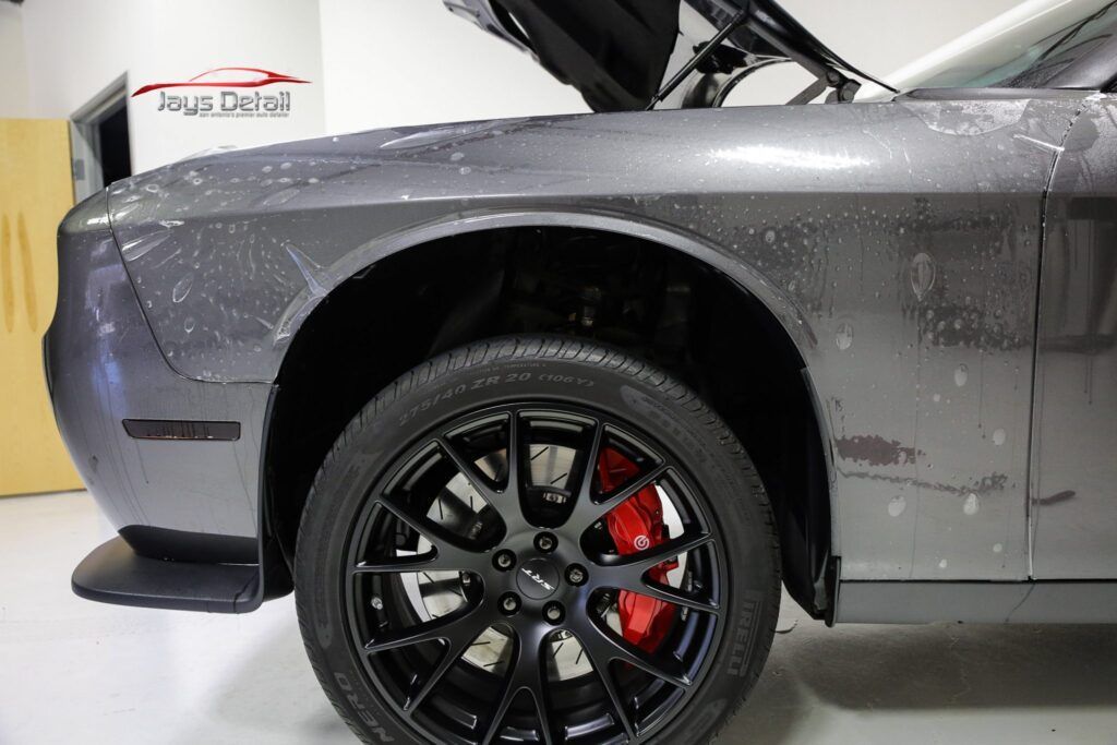 Gray Dodge Challenger front quarter panel with black wheel, red brake calipers, and open hood.