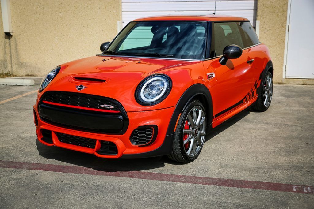 Orange Mini Cooper parked in front of a building with a garage door.