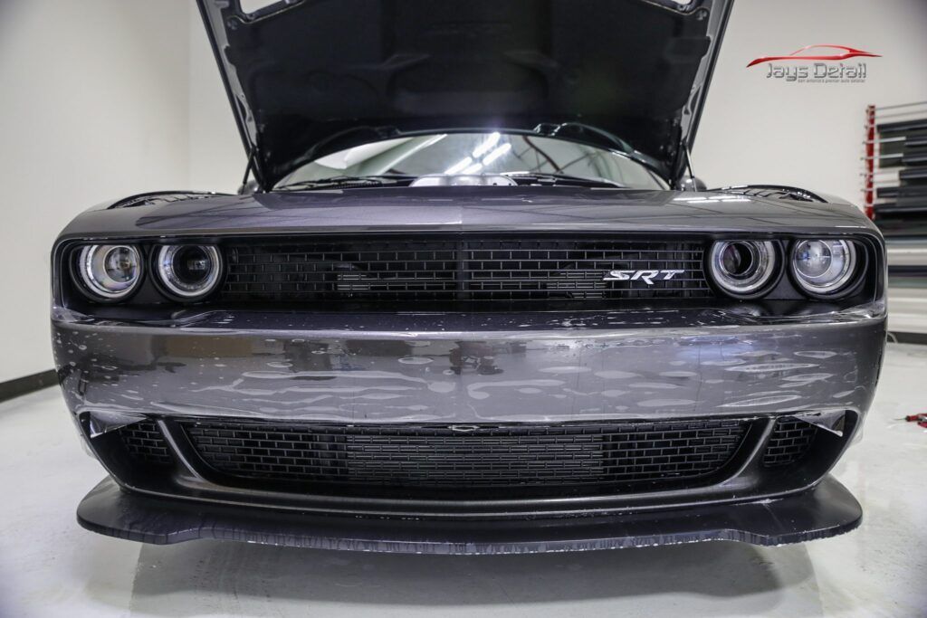 Black Dodge Challenger with open hood, showing front view, in a garage.