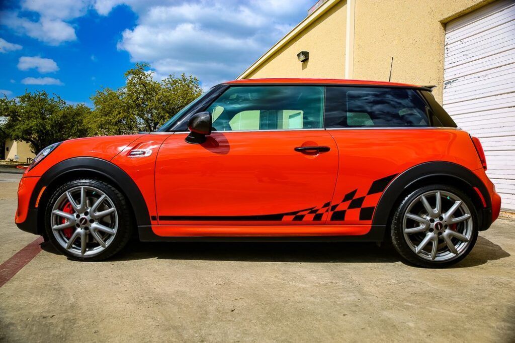 Orange Mini Cooper with checkered side decals, parked outside a building.