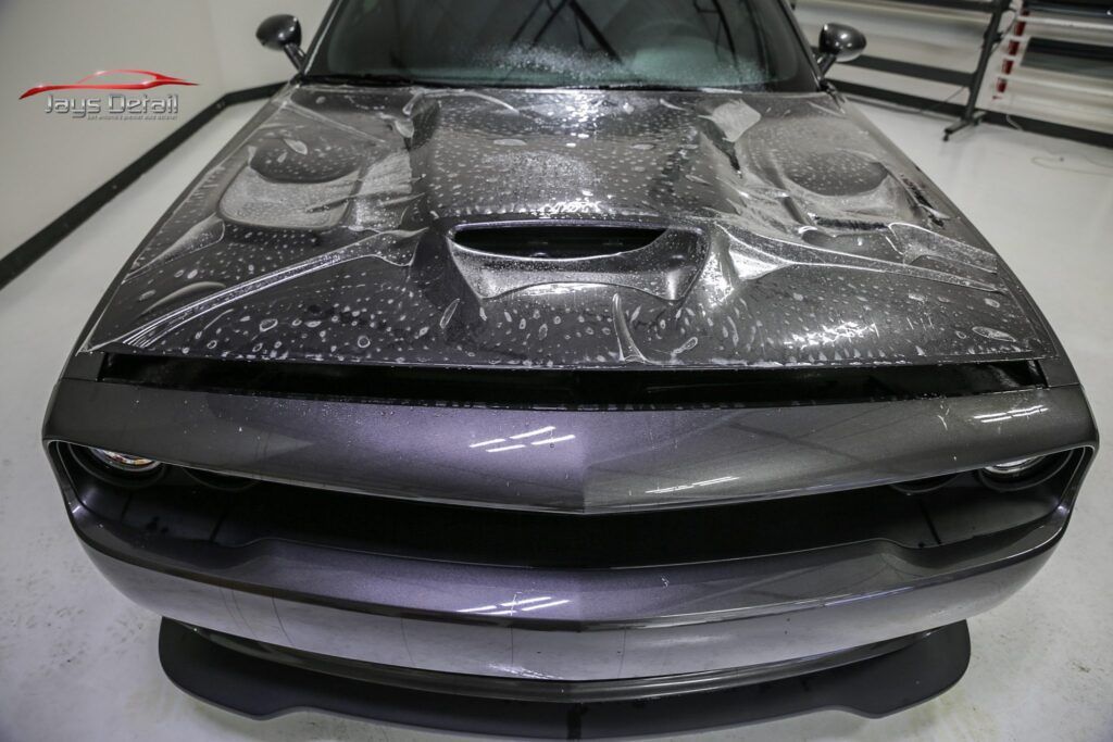 Gray Dodge Challenger with carbon fiber hood in a garage.