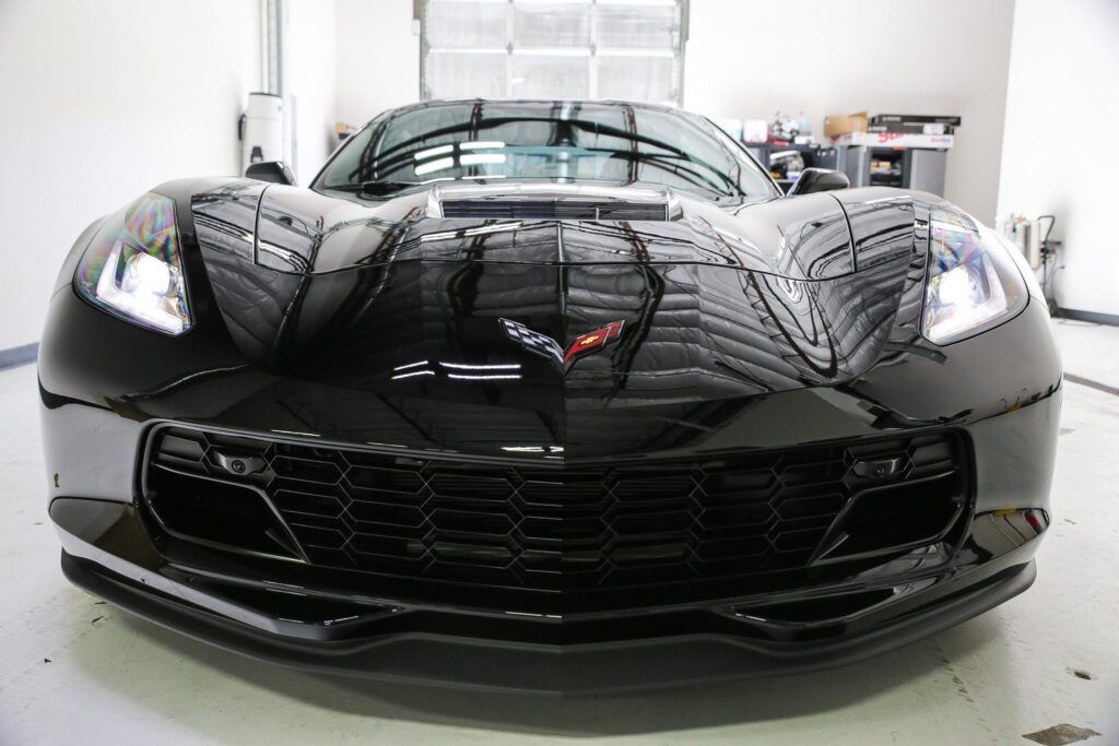Black Corvette sports car, front view, glossy finish, headlights on, indoor setting.