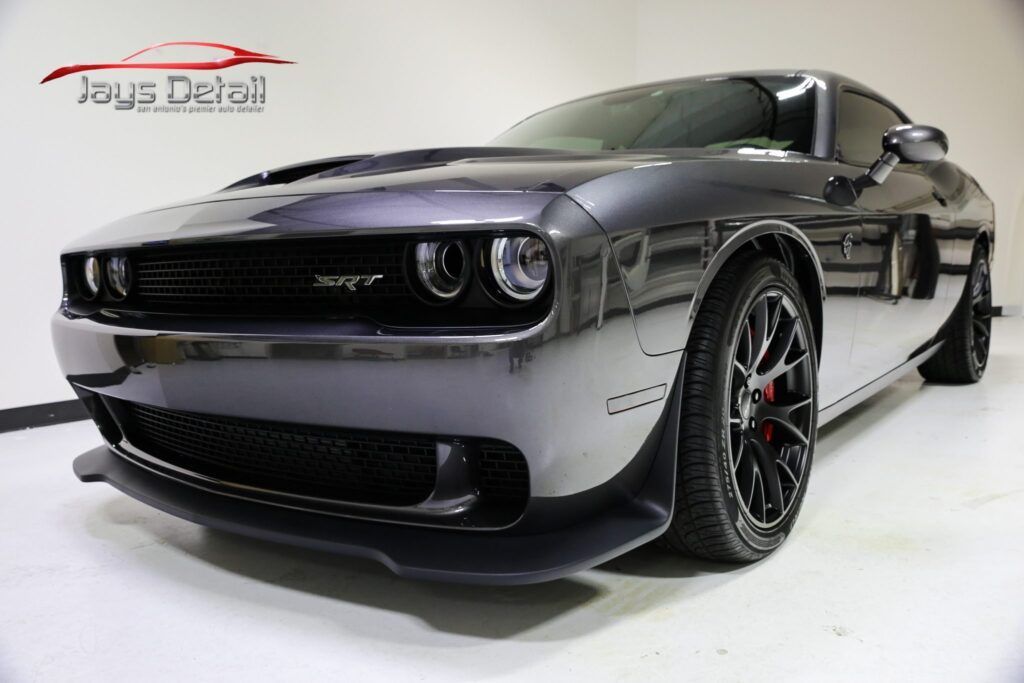 A metallic gray Dodge Challenger SRT, parked indoors, with black wheels and a front spoiler.