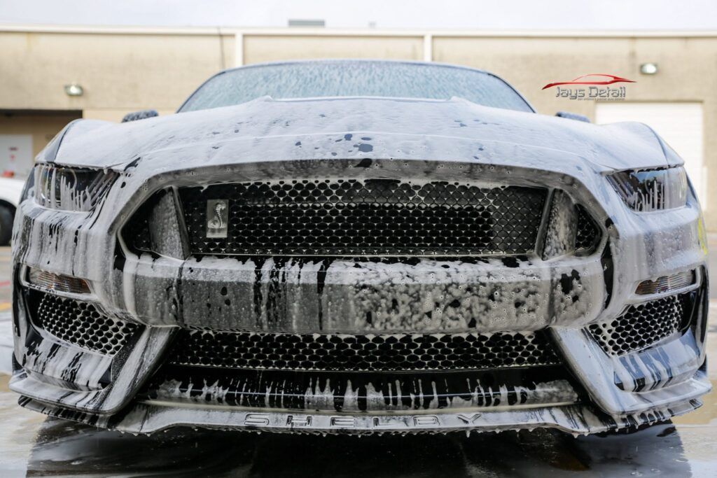 Ford Mustang covered in white foam at a car wash.