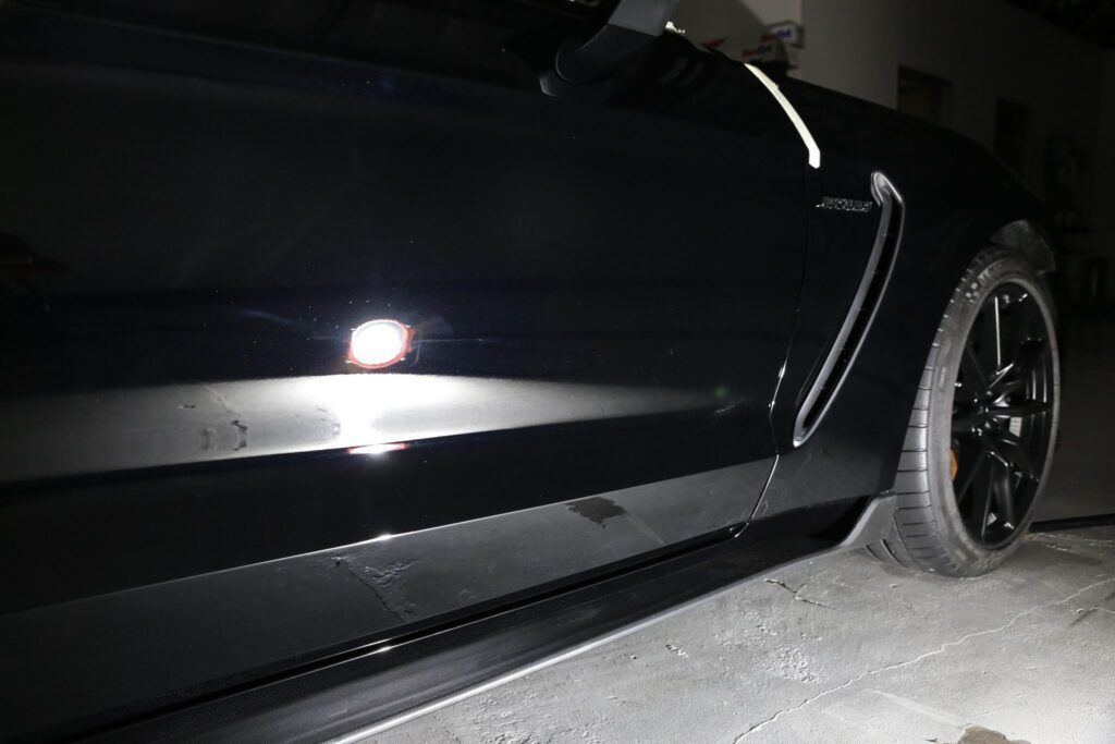 Black sports car, side view, parked at night. Tires and side skirt visible.