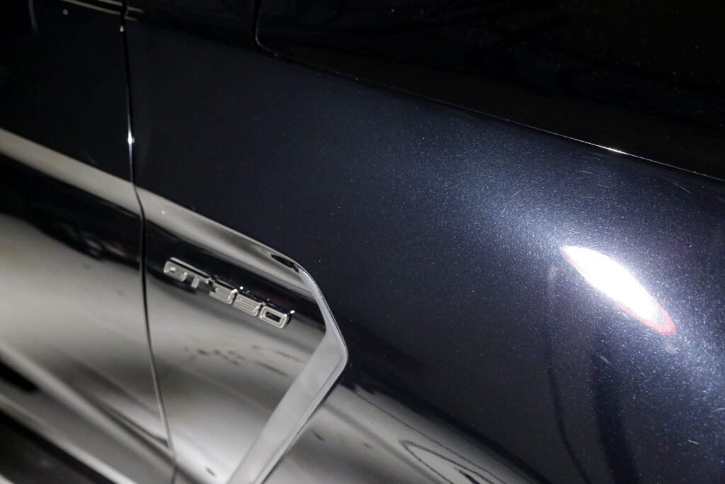 Dark blue car door, with a reflective surface, gleaming under a bright light. Silver trim and a side marker light visible.