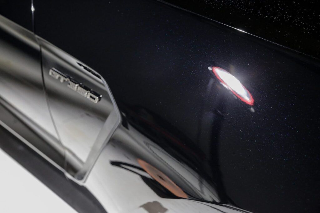 Black car's side panel with a chrome accent and illuminated red light, likely a marker light.