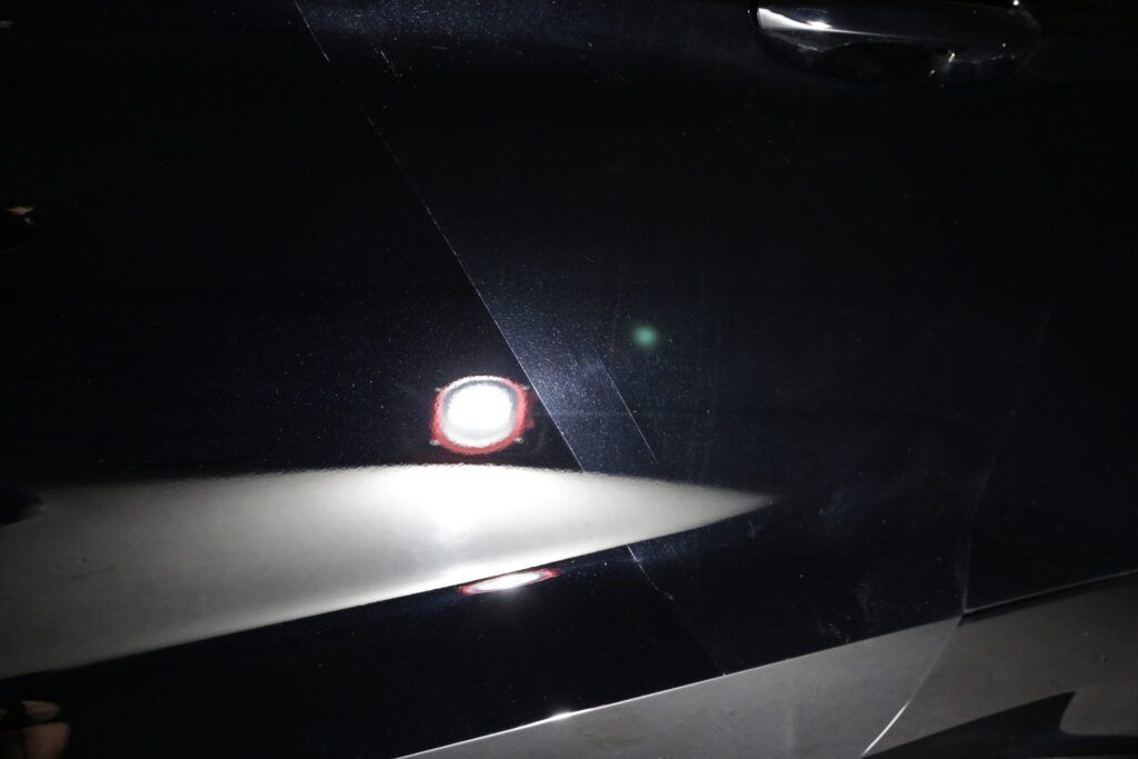 A black car door illuminated by a light, showing a white patch with reddish ring.