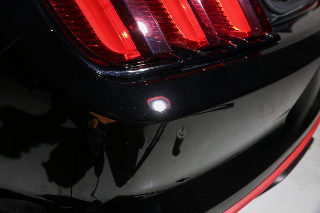 Close-up of a black car's rear bumper with a bright white light and red taillight visible.
