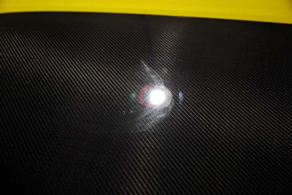 Close-up of glossy black carbon fiber with a bright reflection, yellow background.