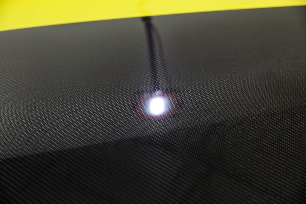 Close-up of a black mesh surface with a bright white reflection in the center.